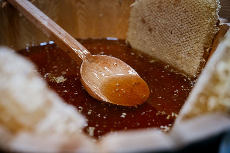Close-up of fresh honey and honeycomb with a wooden spoon in a rustic wooden bowl.