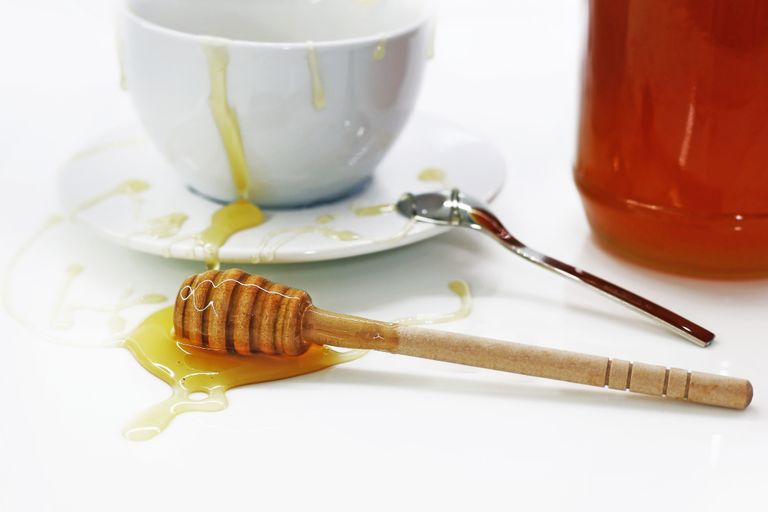Close-up of honey dripping from a wooden dipper and bowl, showcasing sweet indulgence.