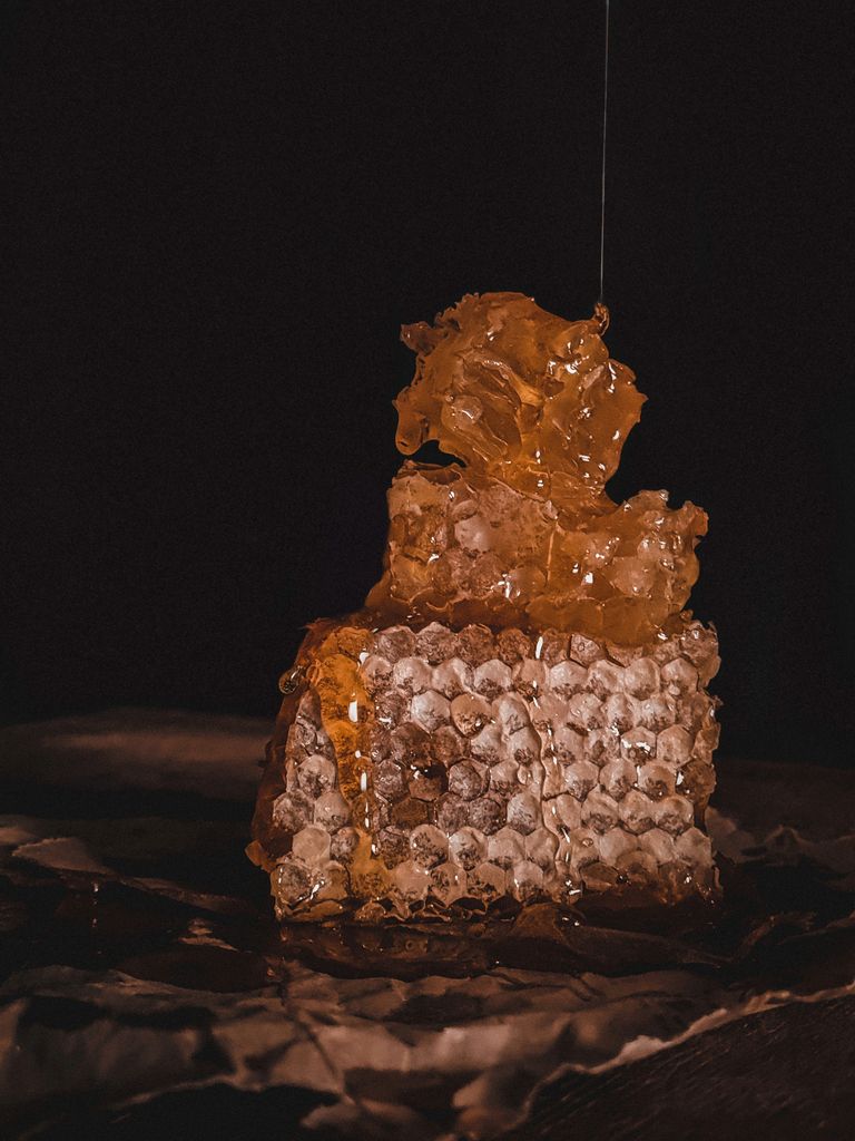 Glistening honeycomb on a dark background with honey dripping.