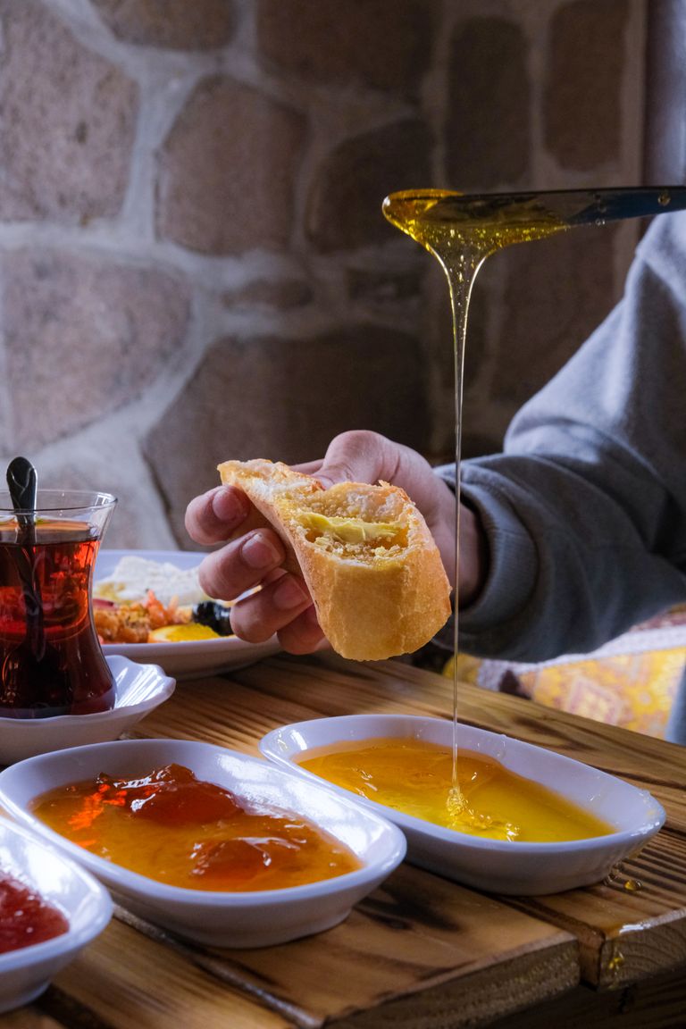Hand pouring honey on bread with a variety of jams, perfect breakfast scene.