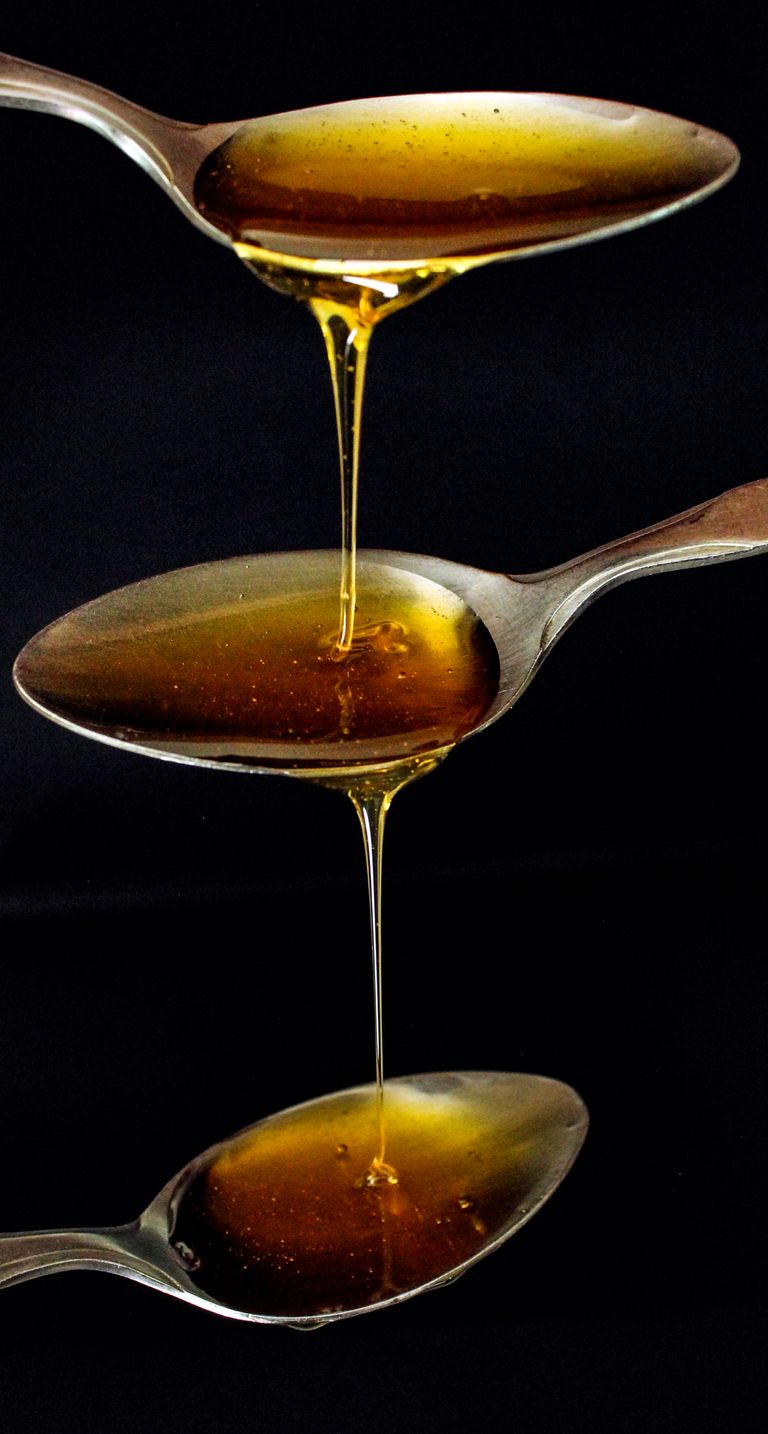 Three spoons with rich golden honey cascading against a black background.