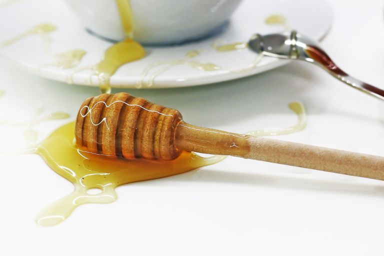 Close-up of a honey dripper with spilled honey on a white surface, creating a sweet mess.