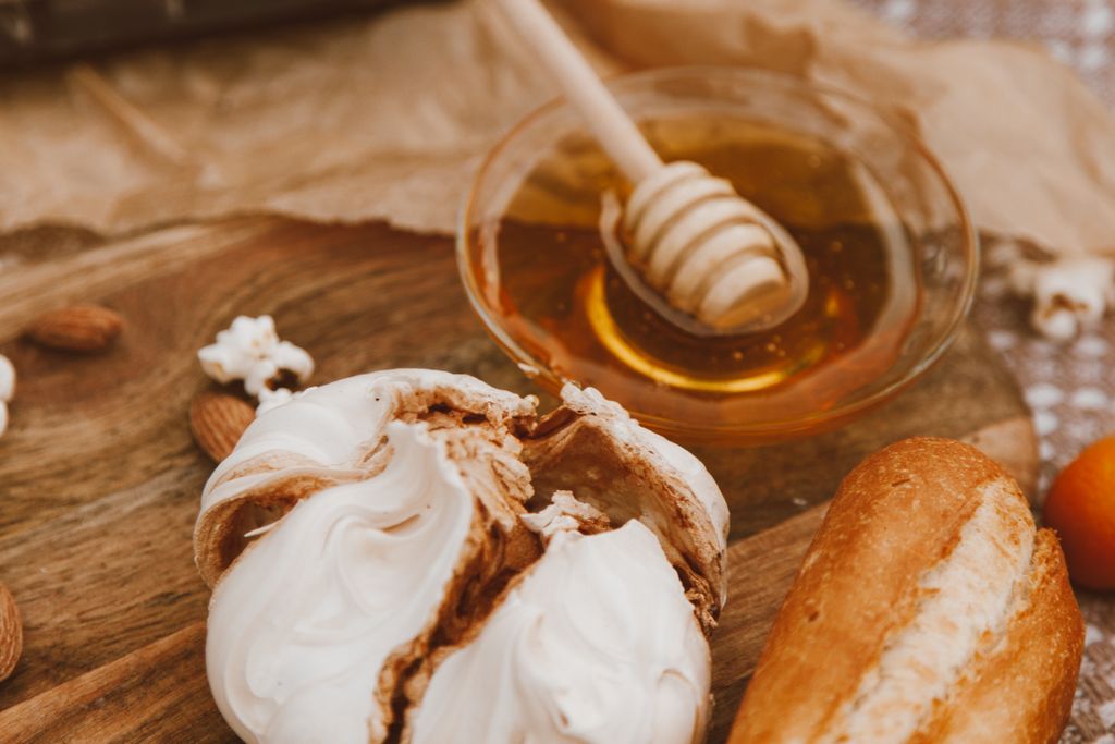 A rustic setting with fresh bread, honey, meringue, and almonds on a wooden table.